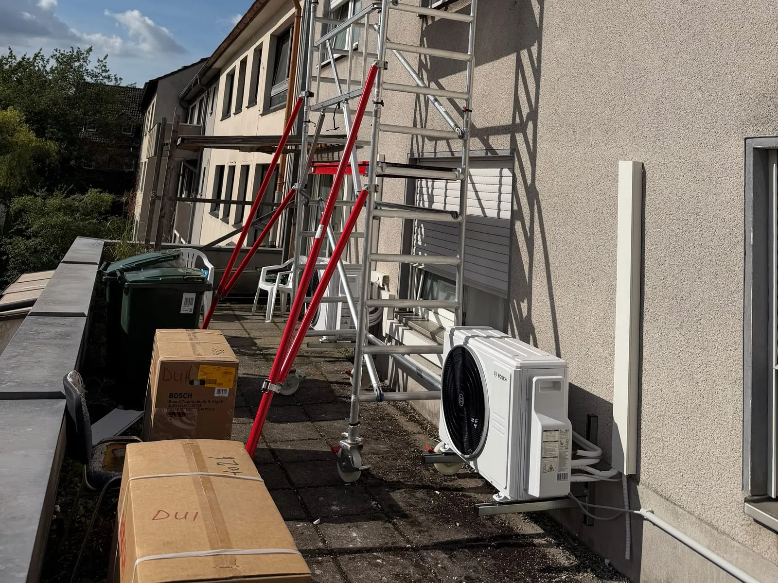Neu montiertes Klima-Außengerät an einer Hauswand, daneben das Montagegerüst